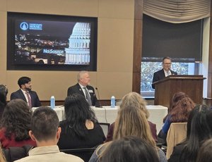 Rep. Gus Bilirakis stands at a podium and speaks to an audience on Capitol Hill. A panel of three people sits to his right.