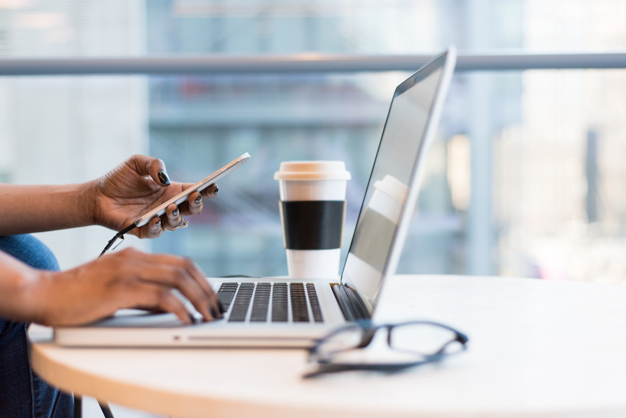 woman holding a phone and working on laptop tech