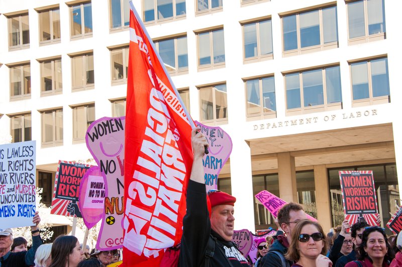 People marching for gender equity and equal pay outside the U.S. Department of Labor, carrying signs, including a sign that says Women Workers Rising.