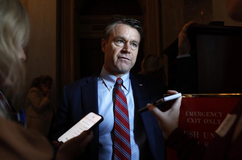 Senator Todd Young speaking to reporters in a hallway, surrounded by reporters.