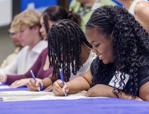 Several youth apprentices are sitting at a table and signing their contracts.