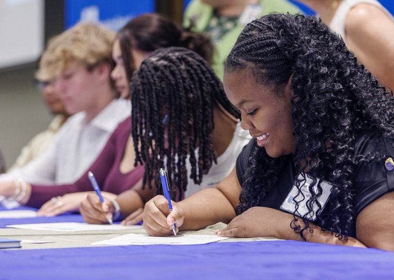 Several youth apprentices are sitting at a table and signing their contracts.