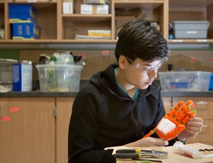 high school student with safety goggles in a lab with a robotic hand