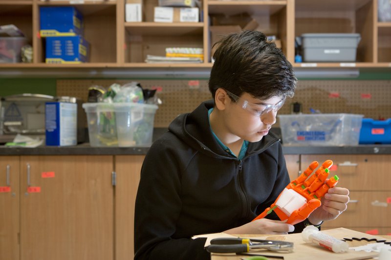 high school student with safety goggles in a lab with a robotic hand