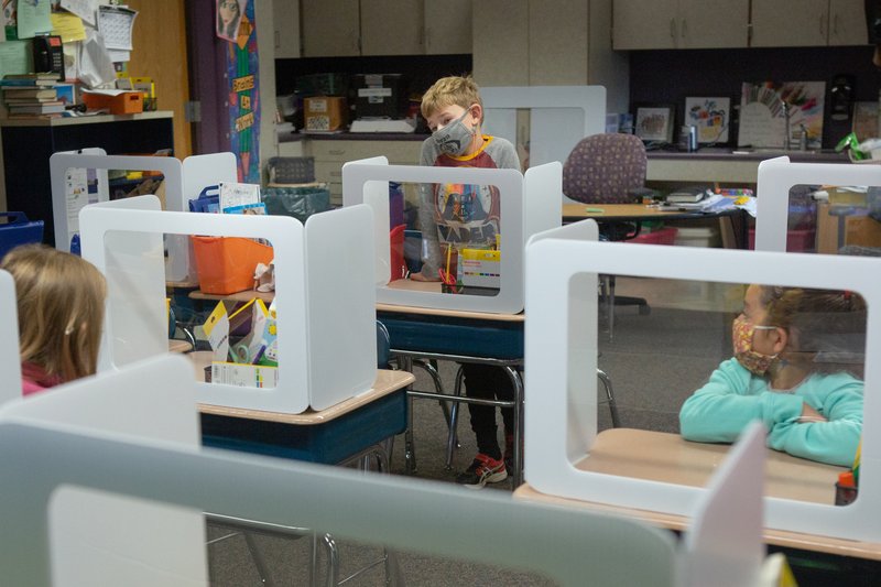 Second-grade students wearing masks sit at desks behind protection shields during the COVID-19 pandemic.