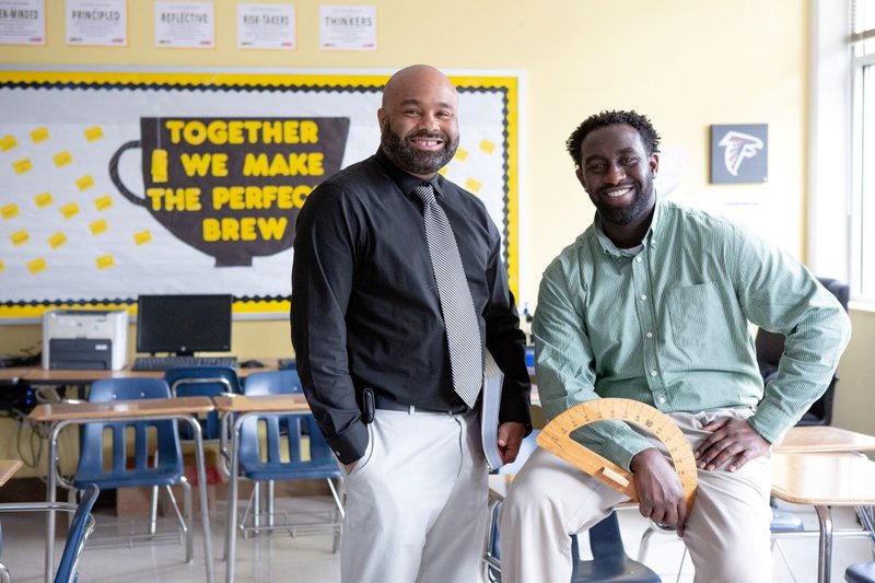 Two Black men sit in a classroom.