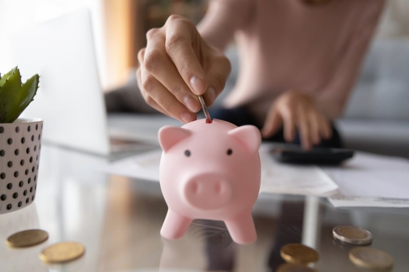 A woman putting coins into a pink piggy bank
