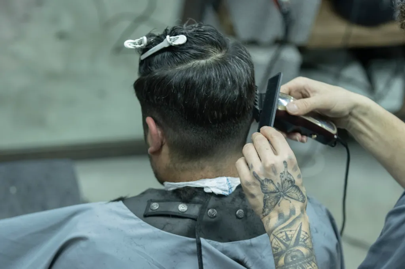 A barber trims a client’s hair with electric clippers, representing students training in beauty and cosmetology programs.