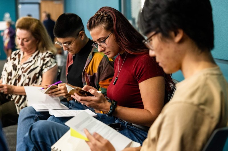 A group of four people sitting in a row, reading and writing.