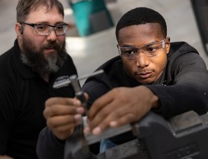 An industrial maintenance mechanic watches as an apprentice mechanic repairs industrial equipment.