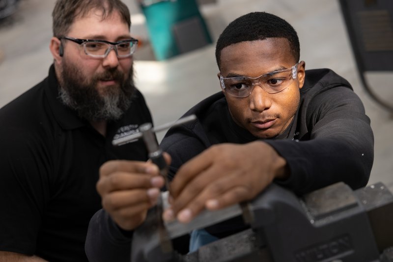 An industrial maintenance mechanic watches as an apprentice mechanic repairs industrial equipment.
