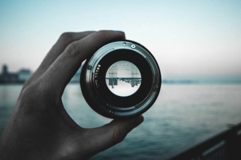 Cropped hand holding lens against sea reflecting Detroit, Michigan cityscape.