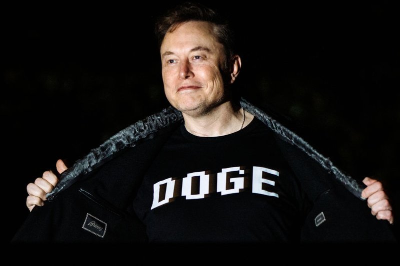 Elon Musk wears a black shirt with the word "DOGE" on it.