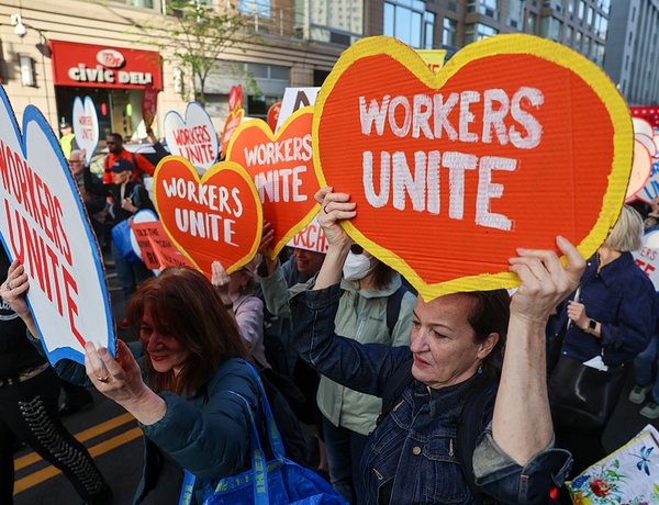 Thousands of people participate in a rally and march on May Day in Manhattan holding “Workers Unite” heart-shaped signs.