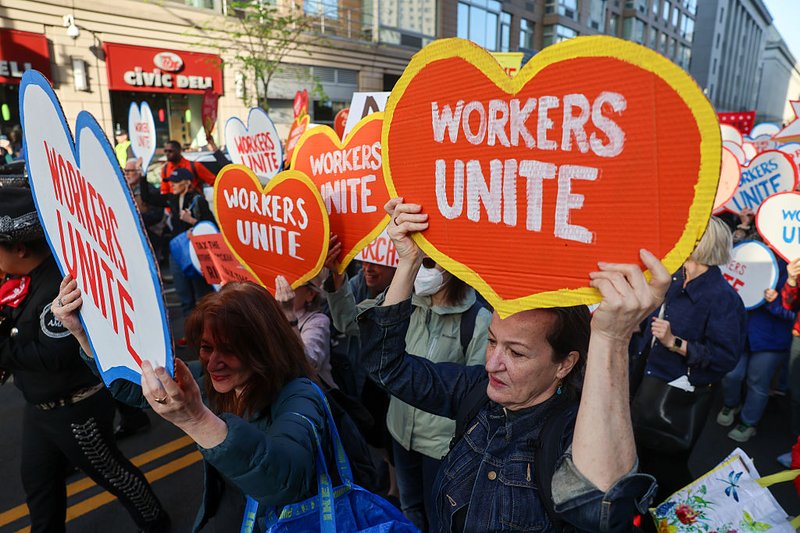 Thousands of people participate in a rally and march on May Day in Manhattan holding “Workers Unite” heart-shaped signs.