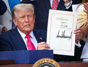 Doland Trump holding a signed piece of paper at a podium