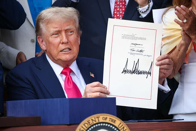 Doland Trump holding a signed piece of paper at a podium