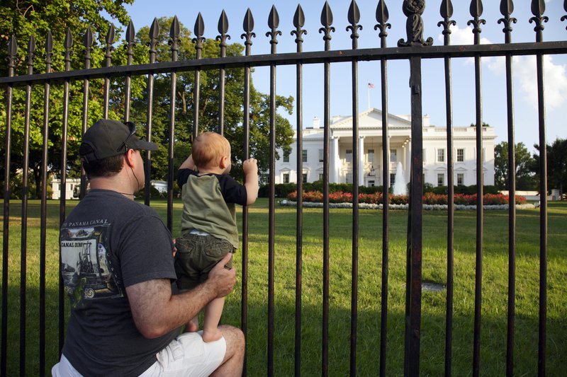 A father has his toddler on his knee just outside the White House gate.