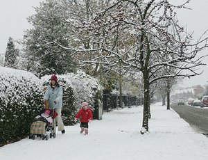 Families walks in a neighborhood and enjoys the winter weather and snow fall.