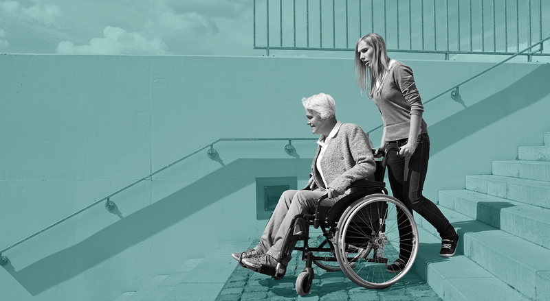 Younger person guides older person in wheelchair at foot of stairs, against teal background.