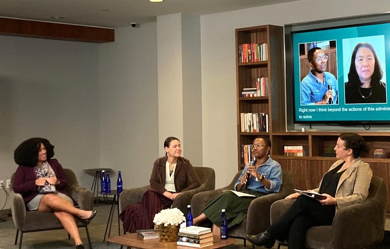 One moderator and three panelists sit in chairs at New America and two are pictured on a large screen as virtual participants.