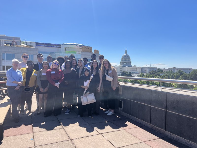 The PAYA Youth Council, a group of 15 young adults, poses for a group photo on the roof of the U.S. Department of Labor. The dome of the Capitol building is visible in the background.