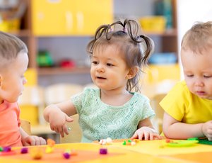 Three preschoolers sit at a table playing with blocks.