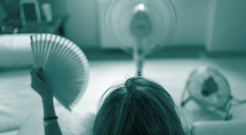 A person holds a paper fan sitting across from two mechanical fans, with a teal overlay.