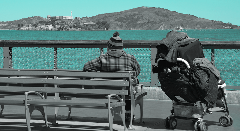 Person sits on bench next to their possessions on a rolling cart, overlooking bay, with teal geometric overlay.