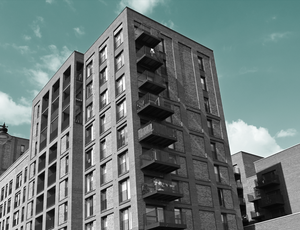 A view looking up at a multistory apartment building, beneath a teal sky.
