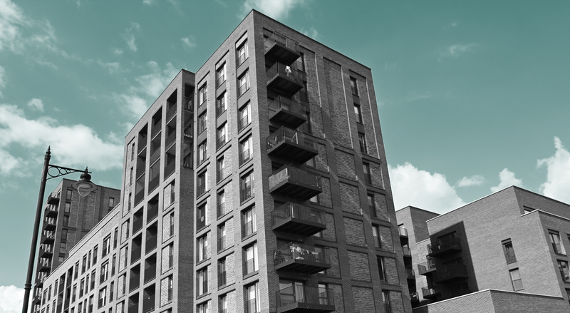 A view looking up at a multistory apartment building, beneath a teal sky.