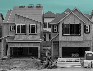 Houses being built next to each other on a street set against a teal sky.