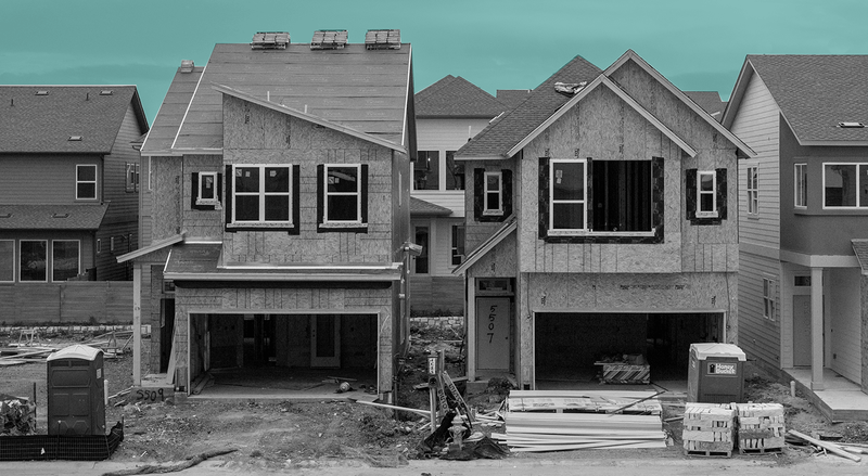 Houses being built next to each other on a street set against a teal sky.