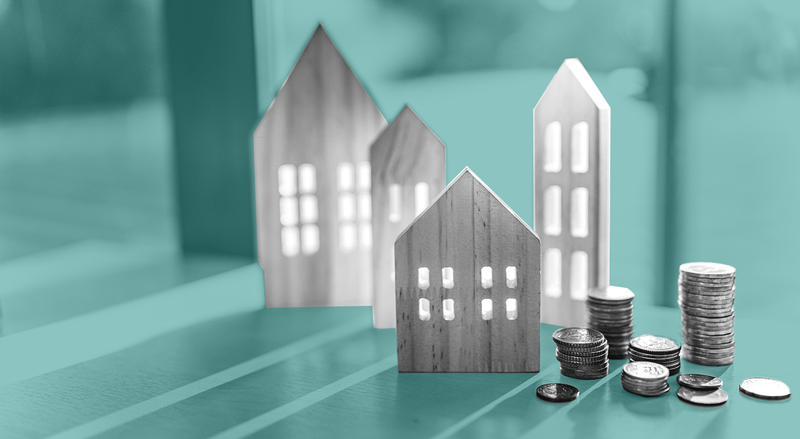 Toy-like housing facades are lined up next to stacks of coins on a table, against a teal background.