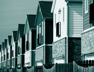 A row of narrow, similar-looking single family homes behind wooden fences, in teal.