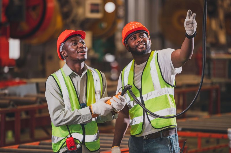 Two men in hazard vests and hard hats working in a shop.