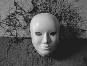 A a white masquerade mask lies on cracked concrete.