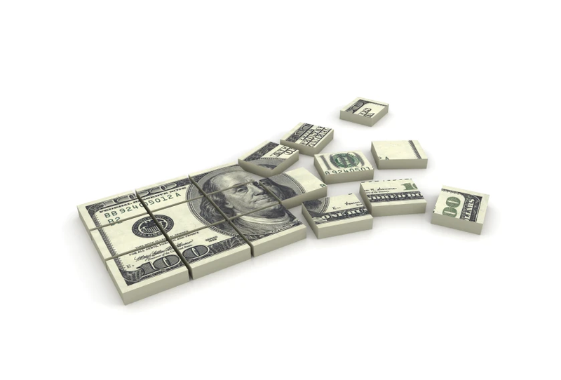 A one-hundred dollar bill is broken into pieces and scattering