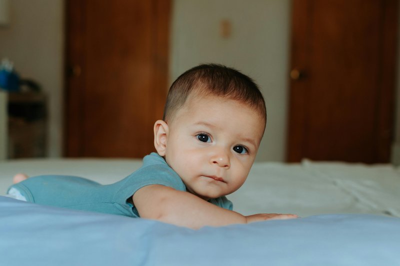 An infant lies on his stomach with his face looking up.
