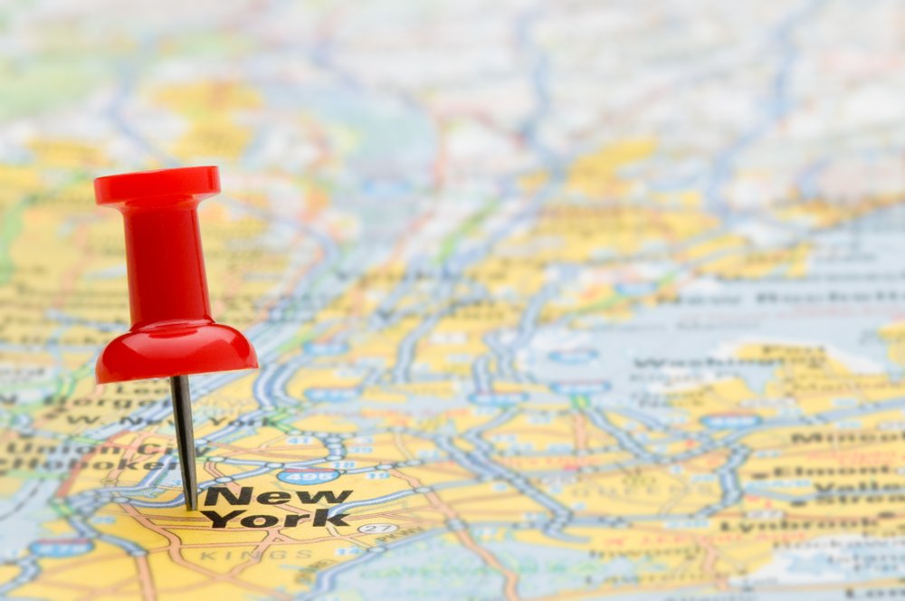 Image of a yellow geographic map with a red pushpin near the words "New York"