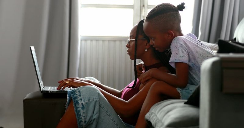 Person and child sitting on a couch, looking at a laptop together.