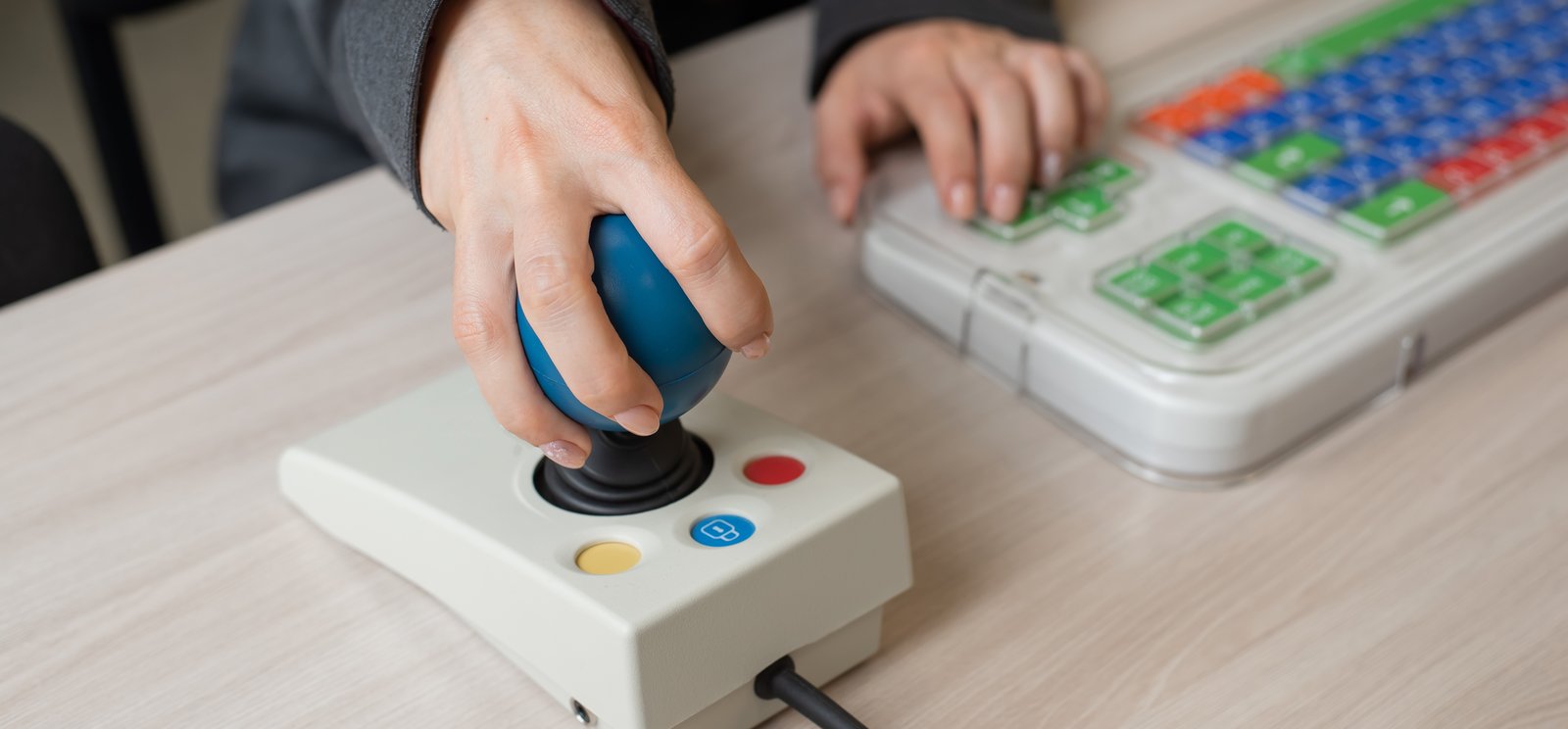 Close-up of a person's hands using a special color-coded keyboard and joystick at desk.
