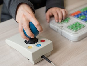 Close-up of a person's hands using a special color-coded keyboard and joystick at desk.