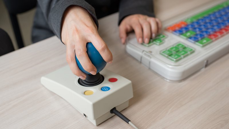 Close-up of a person's hands using a special color-coded keyboard and joystick at desk.