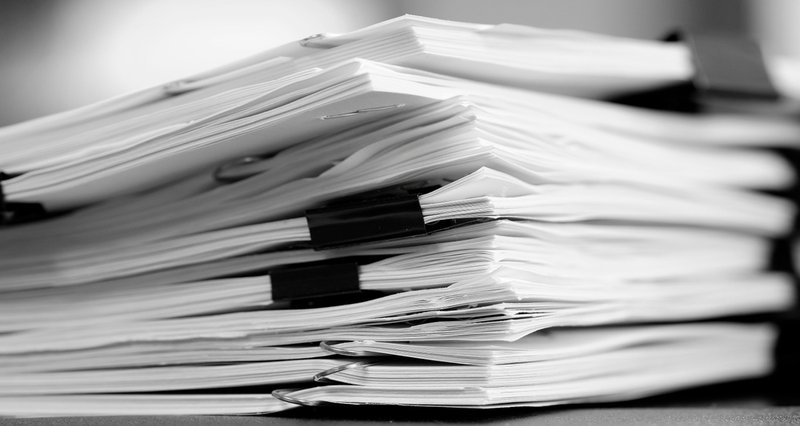 The image is an up close shot of stacks of paper held together by binder clips.