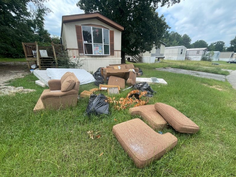 Furniture and other belongings are strewn in the grass outside a manufactured home.