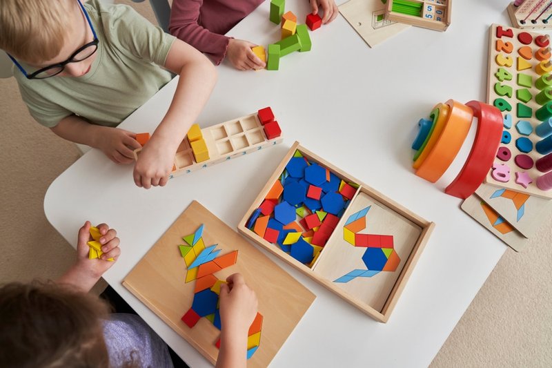 Children playing with colorful geometric blocks and educational toys at a white table.