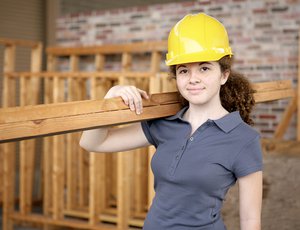 young female youth apprentice working on construction job site holding wooden beams