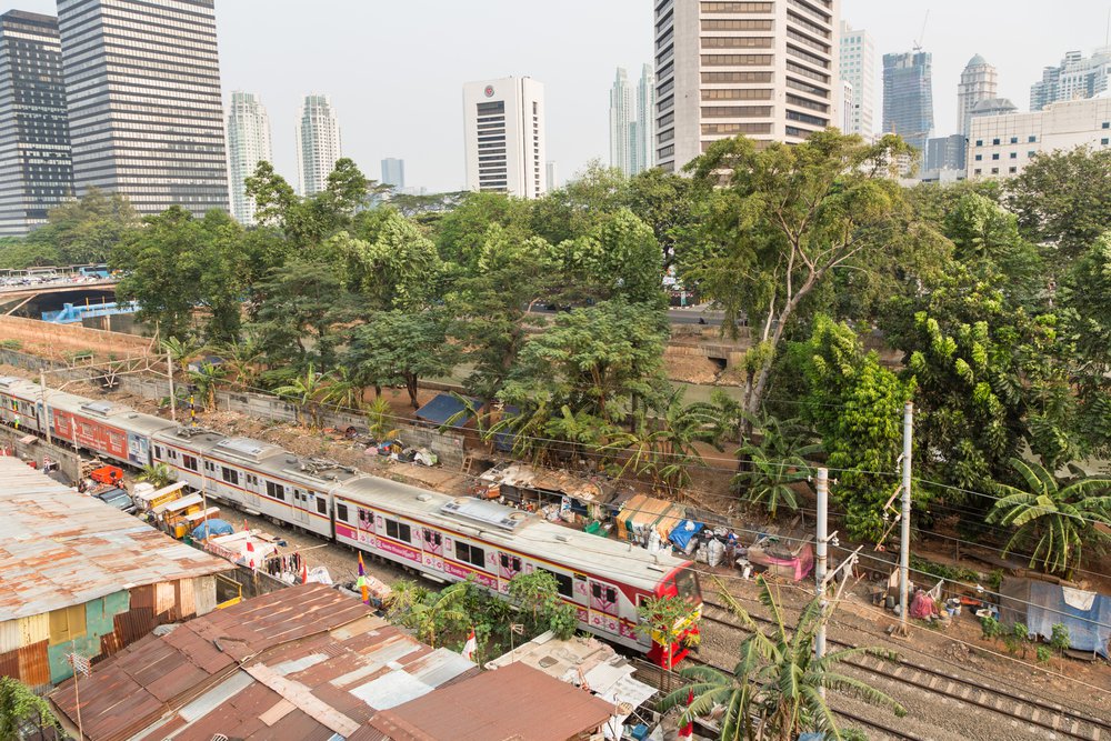 JAKARTA, INDONESIA - AUGUST 21 2015: A commuter train goes through a shanty town right next to the business district of Jakarta, where poverty contrasts with modern office in the background.