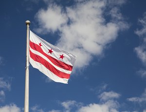The flag of the District of Columbia waves against a blue sky with clouds